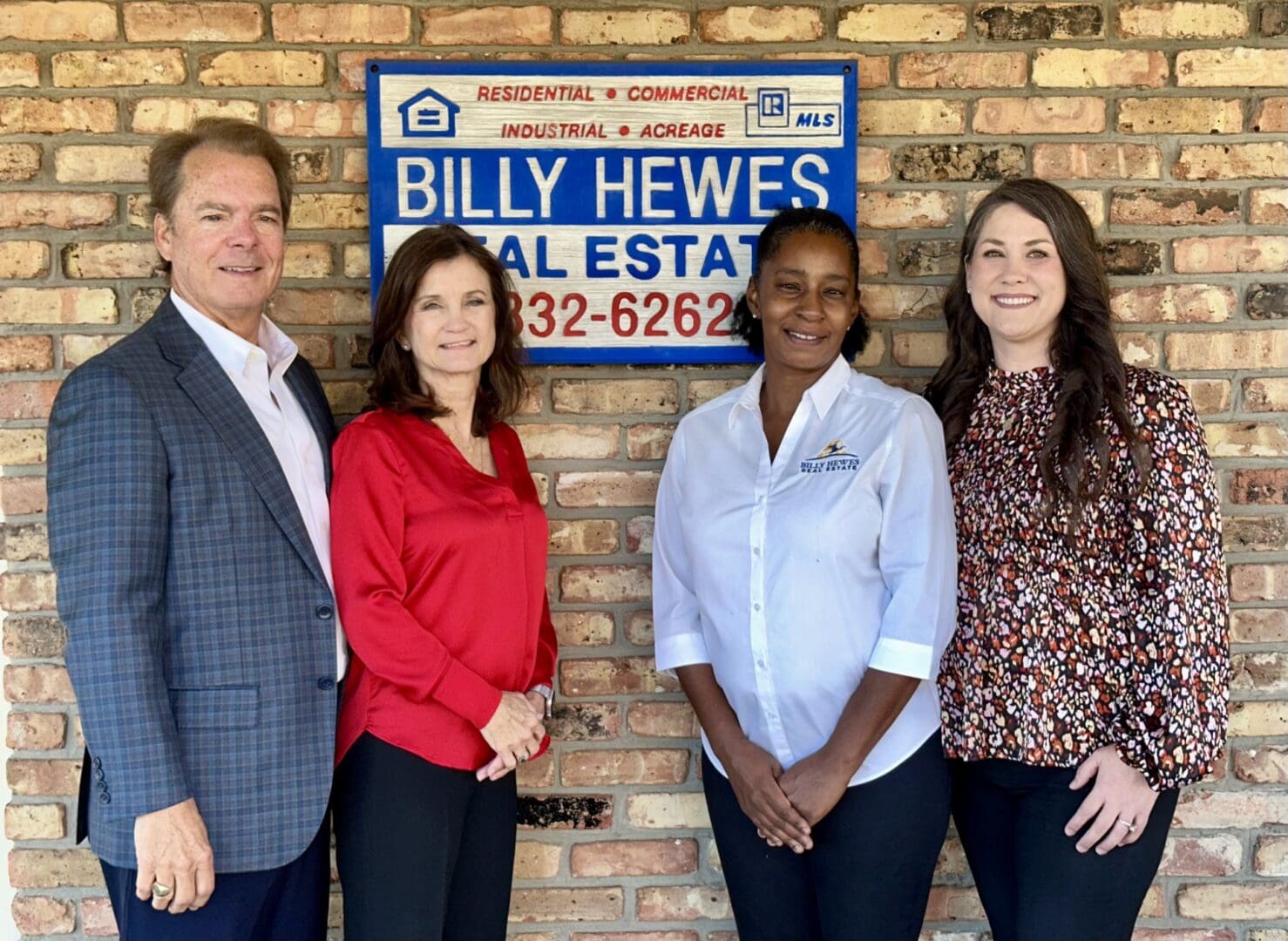 Four real estate agents stand in front of a Billy Hewes Real Estate sign.