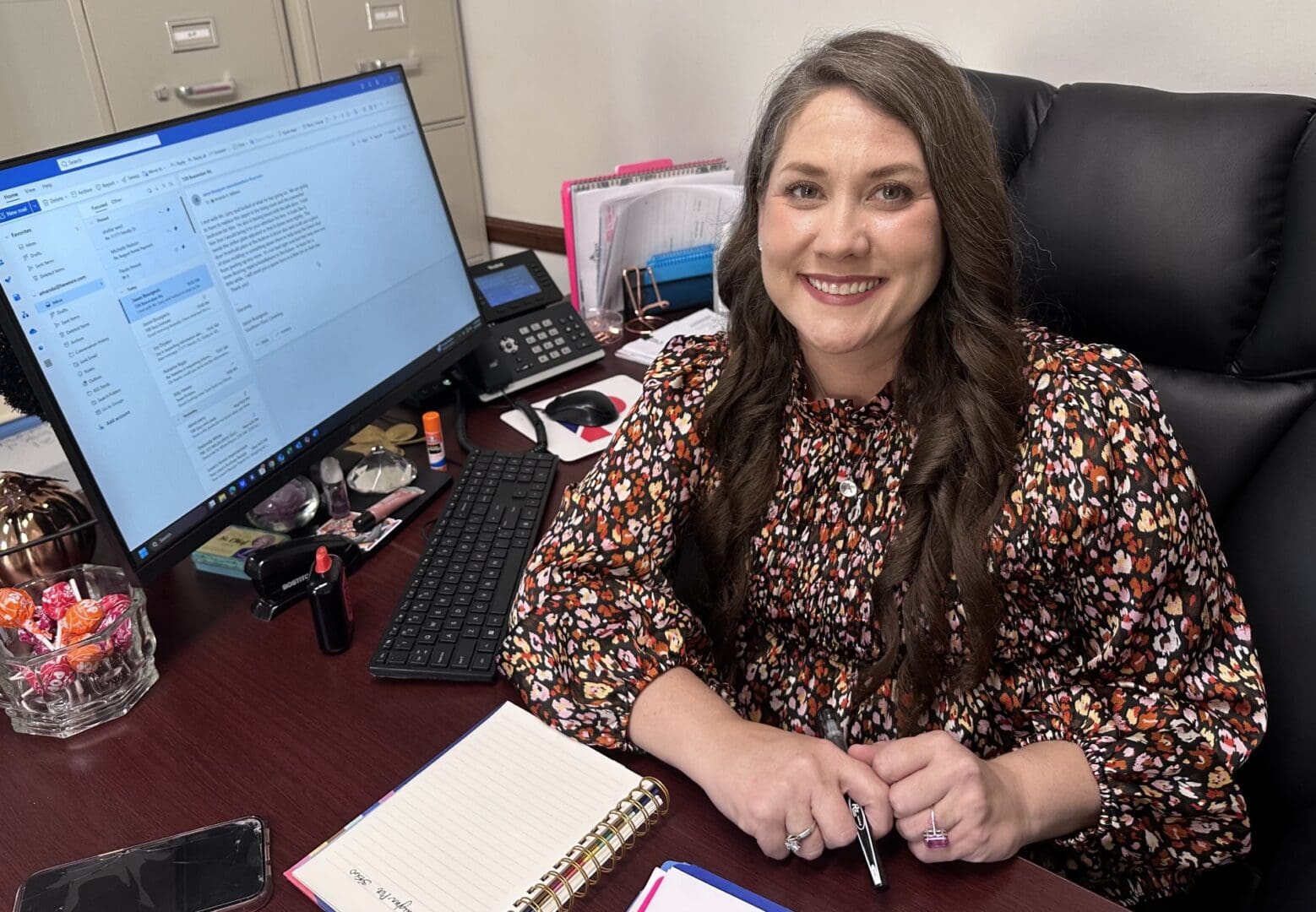 Smiling woman sitting at a desk with a computer and planner.